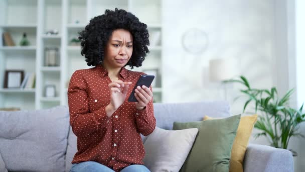沮丧的非洲裔美国女性抱怨家里坐在沙发上的智能手机节目表现不佳 黑人妇女对手机 互联网或服务的工作不满意 — 图库视频影像