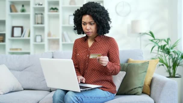 沮丧的年轻非洲裔美国女性在家里客厅的笔记本电脑上输入信用卡号码时发现了欺诈行为 悲哀的黑人妇女看到钱从她的帐户上被偷了 — 图库视频影像