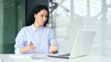 Kendine güveni tam genç bir bayan çalışan modern bir ofiste çalışan bir dizüstü bilgisayarla video görüşmesi yapıyor. İnternetteki bir konferansta konuşan kadın. Koç, danışman veya danışman danışmanlık yapar
