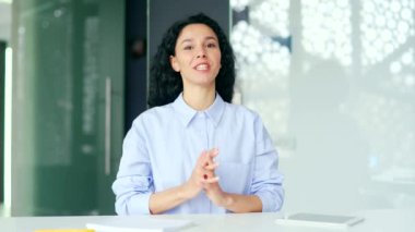 Webcam görüntüsü. Genç bayan çalışan, modern bir ofiste iş yerinde kameraya bakarak bir video görüşmesinde konuşuyor. Kendine güvenen koç uzaktan konuşur, çevrimiçi bir konferansta bir konuşma yapar.