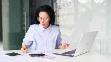 Meşgul genç bayan muhasebeci bilgisayarla, hesap makinesiyle uzaktan çalışıyor, iş yerinde otururken notlar alıyor. Gözlüklü kendine güvenen muhasebeci modern ofiste hesap açar.