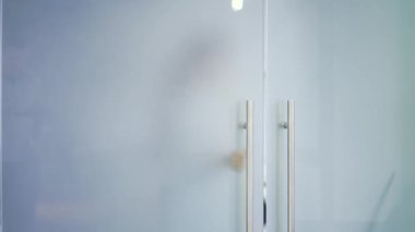 Mavi gömlekli genç bir bayan modern bir binada cam bir kapı açar ve ofisten salona doğru yürür. Kendine güvenen kıvırcık saçlı esmer iş kadını iş yerini terk edip kapalı bir toplantıya gidiyor.