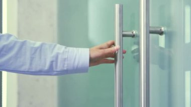 Modern bir binada cam ofis kapısını açan metal kapı tokmağını tutan bir kadının fotoğrafını çek. İş kadını ya da gömlekli bir çalışan kapıyı açar ve işyerine gider.