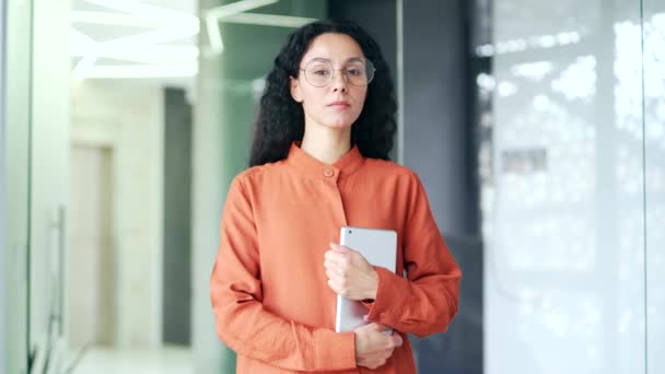 一个年轻自信的女员工手持石碑站在现代化的办公室里的画像 严肃的卷曲黑发女人 戴着眼镜看着相机 一个成功的女商人的头像 — 图库视频影像