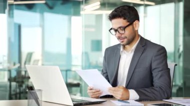 Resmi bir takım elbise içindeki heyecanlı finansör, bir iş yerinde otururken incelediği mali raporun sonuçlarından memnun. Girişimci olumlu göstergelerden memnun