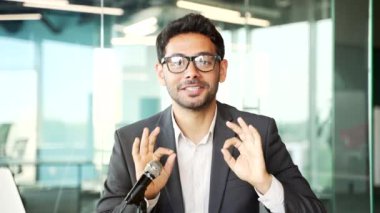 Webcam görüntüsü. Genç işadamı, iş yerinde mikrofon kullanarak bir video konuşması ya da podcast 'i kaydediyor. Erkek koç çevrimiçi bir konferansta uzaktan konuşuyor, kameraya bakıyor.
