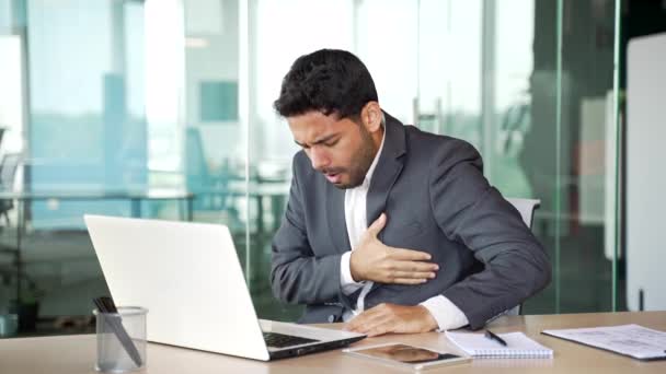 スーツの若いビジネスマンは ビジネスオフィスの職場に座っているラップトップに取り組む心臓発作を起こしています 病気の起業家は胸の緊張に苦しみ 彼の手で痛みのスポットを保持しています — ストック動画