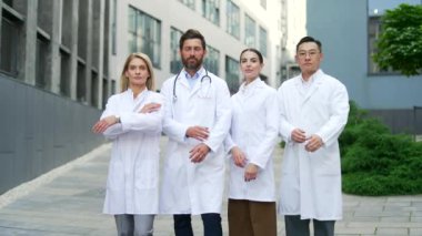 Bir hastane ya da klinik binasının yakınındaki, dışarıda poz veren, kendine güvenen ciddi tıbbi çeşitlilikte sağlık personeli kamerasına bakan doktor, sağlık çalışanı ya da bilim adamlarının portresi.
