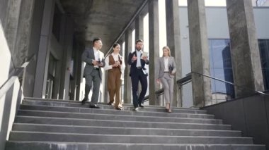 İş adamlarından oluşan bir iş adamı ekibi merdivenlerdeki ofis binasının yanında yürüyor. Resmi takım elbiseli bir grup iş adamı dışarıda konuşuyorlar ve iletişim kuruyorlar.