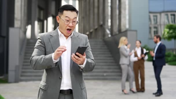 兴高采烈的亚洲商人在电话上收到好消息 庆祝胜利 并取得了重大成果 心满意足的男人看到外面站在城市街道上的智能手机会有积极的反应 — 图库视频影像