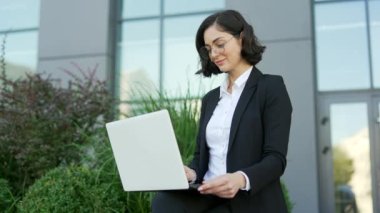 Resmi takım elbiseli genç bir iş kadını, bir ofis binasının yanındaki bankta otururken dizüstü bilgisayarla çalışıyor. Serbest çalışan kadın bir istemci bir istemciyle çevrimiçi sohbet ediyor, e- postaları kontrol ediyor veya mesaj yazıyor