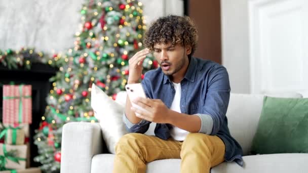 闷闷不乐的英俊男子在新年假期坐在家里用智能手机读坏消息 忧心忡忡的男性在手机上看到消极的信息时很伤心 — 图库视频影像