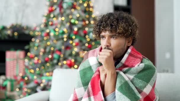 冬のクリスマス休暇中に家でリビングルームでソファーに座っている毛布で覆われた若いハンサムな男 屋内で冷たい男性 男は低温のために不快感を感じる — ストック動画