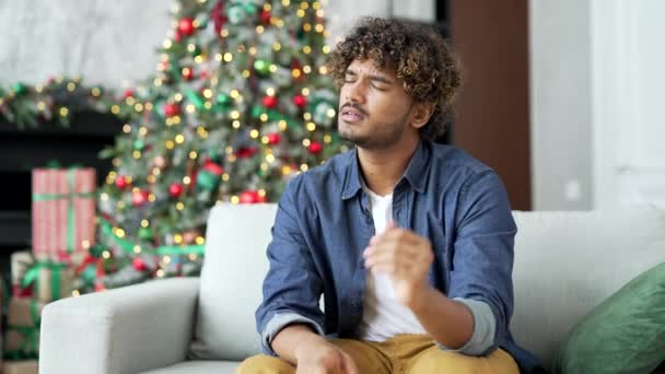 エラシュ 病気の若者は 冬の新年のクリスマス休暇中に家のリビングルームでソファーに座って耳の痛みに苦しんでいます ウプセットの男は 怒りを持っています シングル 耳疾患 耳炎メディア — ストック動画