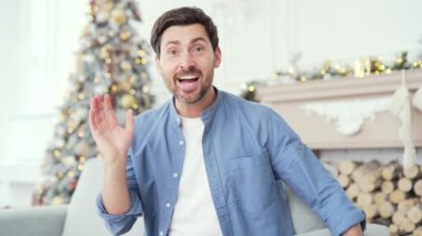 Webcam görüntüsü. Gülümseyen adam, yılbaşı Noel tatilinde evdeki kanepede otururken video görüşmesinde sohbet ederken hediye kutusu gösteriyor. Dilek dileyen mutlu adam, uzaktan tebrik ediyor.
