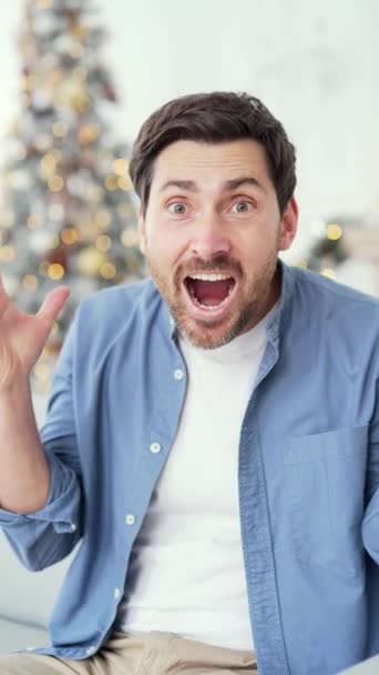垂直录像 圣诞佳节期间 快乐的男人在家里的荧幕上用相机看到了好消息 兴奋的男性看到有关圣诞节销售 折扣或促销的信息 — 图库视频影像