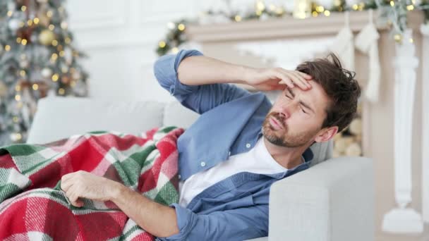 冬のクリスマスXmas休暇中に家でソファーに横たわっているハングルーに苦しんでいる男 毛布で覆われた男性は パーティーを祝った後に吐き気を感じます — ストック動画
