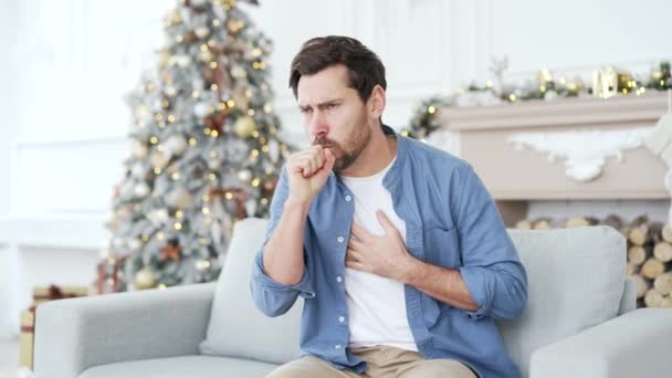 圣诞佳节期间 患感冒或流感的病人坐在家里沙发上咳嗽 心烦意乱的男人把他的手放在胸前他有肺炎或支气管炎 — 图库视频影像