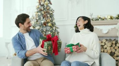 Mutlu çift, yeni yıl Noel Noeli boyunca evdeki oturma odasındaki kanepede otururken birbirlerine hediyeler hazırlıyor. Gülümseyen adam ve kadın hediyeler ve sürprizlerle kutuları değiştiriyor.