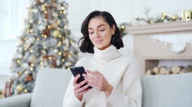 Mutlu, heyecanlı genç kadın, yılbaşı Noel tatilinde evdeki koltukta otururken akıllı telefondan harika haberler aldı. Kız telefonda hoş bir mesaj okuyor, başarıyı kutluyor.