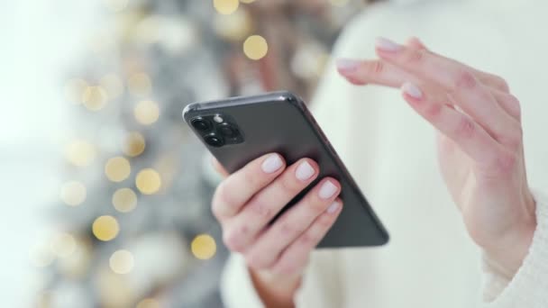 Ferme là. La main de la femme tient un smartphone à la maison pendant les vacances du Nouvel An d'hiver. Femme fait du shopping dans une boutique en ligne pour les rabais de Noël, les ventes et les promotions à l'aide d'un téléphone mobile dans le centre commercial