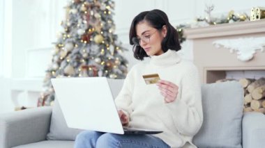 Mutlu bir kadın, yılbaşı Noel tatilinde evde oturup bilgisayarında kredi kartı numarasını yazarak online alışveriş yapıyor. Kadın satın alıyor, promosyon ve indirimlerle tatmin oluyor.