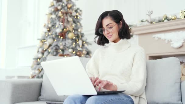 圣诞佳节期间 快乐而兴奋的年轻女子坐在沙发上 在笔记本电脑上收到了好消息 女孩在电脑上看到一个愉快的信息 庆祝成功 — 图库视频影像