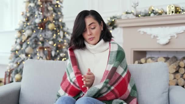 冬のクリスマスXmas休暇中に家のリビングルームでソファーに座っている毛布で覆われた若い女性 屋内で冷たい女性 女の子は低温のために不快感を感じる — ストック動画