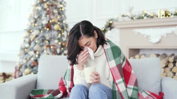 圣诞佳节期间 患感冒或流感的生病妇女坐在家里沙发上咳嗽 用毯子包裹的女性用手帕擦拭鼻子 喝热茶 — 图库视频影像