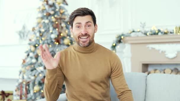 ウェブカメラビュー ハッピーハンサムな男は 冬のクリスマスXmas休暇中に自宅のリビングルームでソファーに座っているビデオ通話で話しています 笑顔の男性の話す願い リモートでお祝い — ストック動画