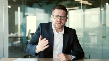 Webcam görüntüsü. Resmi takım elbiseli kızgın bir işadamı iş yerindeki bir iş yerinde konuşurken görüntülü konuşuyor. Heyecanlı erkek patron, kameraya bakan sorunlardan duygusal olarak bahsediyor.