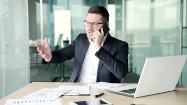 Resmi takım elbiseli kızgın işadamı iş yerinde otururken akıllı telefon kullanarak tartışıyor. Heyecanlı erkek patron, bir astıyla sorunlar hakkında duygusal olarak konuşur.