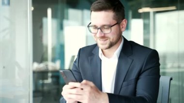 Resmi takım elbiseli bir işadamı iş yerindeki akıllı telefonu kullanıyor. İşçi iletileri okur veya yazar, bir istemciyle sohbet eder, sosyal ağlara göz atar, e- postaları kontrol eder veya çevrimiçi alışverişleri yapar