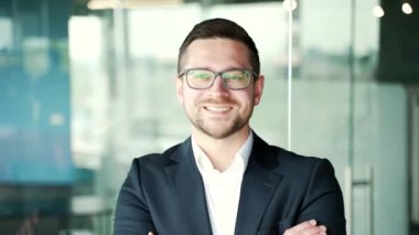 Kapatın. İş yerinde duran takım elbiseli ve gözlüklü başarılı bir iş adamının portresi. Kameraya bakarak poz veren kendine güvenen güler yüzlü girişimci. Müdürün kafasından.