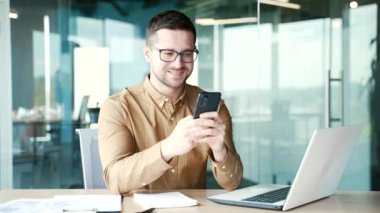 İşadamı iş yerindeki iş yerinde akıllı telefon kullanıyor. Girişimci mesajları okur veya yazar, bir istemciyle sohbet eder, sosyal ağlara göz atar, e-postaları kontrol eder veya çevrimiçi alımlar yapar