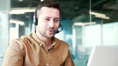 Kapatın. Ofisteki bir iş yerinde otururken, kulaklıkla gülümseyen genç bir iş adamı bir video görüşmesinde konuşuyor. Olumlu bir girişimci iş görüşmesi yapar, çevrimiçi bir konferansta uzaktan konuşur.