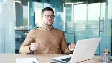 Genç bir iş adamı, bir iş yerinde iş yerinde otururken gözleri kapalı meditasyon yapıyor. Sakin ve yakışıklı bir işçi huzur içinde yatar. Erkek stres atmak için rahatlatır.