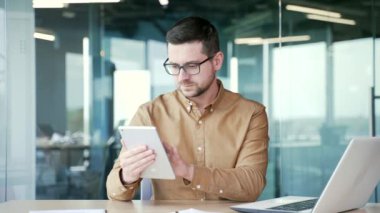 İşadamı iş yerindeki iş yerinde tablet kullanıyor. Girişimci bir iletiyi okuyor veya yazıyor, bir istemciyle sohbet ediyor, sosyal ağlara göz atıyor, e-posta veya alışverişi çevrimiçi olarak kontrol ediyor
