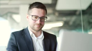 Kapatın. İş yerindeki bir iş yerinde otururken dizüstü bilgisayarda yazı yazan resmi takım elbiseli bir iş adamı. Gözlüklü, kendine güvenen bir girişimci bilgisayar üzerine bir başlangıç projesi üzerinde çalışıyor.