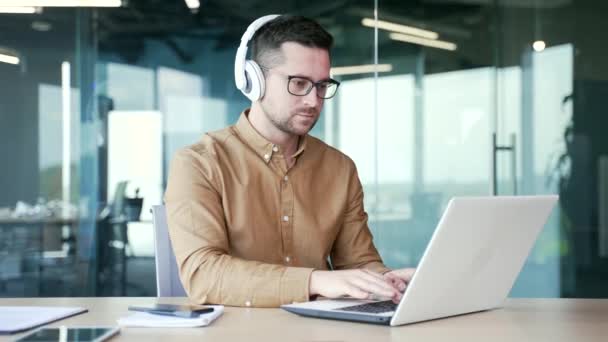 자신감있는 프로그래머는 비즈니스 사무실에서 직장에 앉아있는 노트북에 코드를 씁니다 헤드폰에서 — 비디오