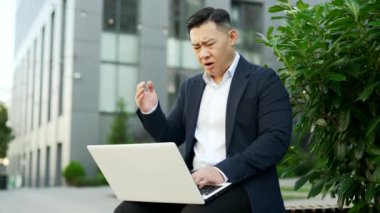 Resmi takım elbiseli endişeli Asyalı işadamı ofis binasının yakınındaki bir bankta otururken dizüstü bilgisayardan kötü haberler okudu. Sinirli girişimci kötü bir ruh hali içinde, mesaja bakıyor.
