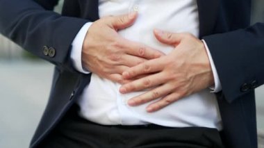 Kapatın. Erkek eller karın okşayarak masaj yapıyor. Sokakta bir bankta otururken karın ağrısı çeken resmi takım elbiseli bir adam. Zehirlenme, kabızlık, mide ekşimesi ya da aşırı yeme.