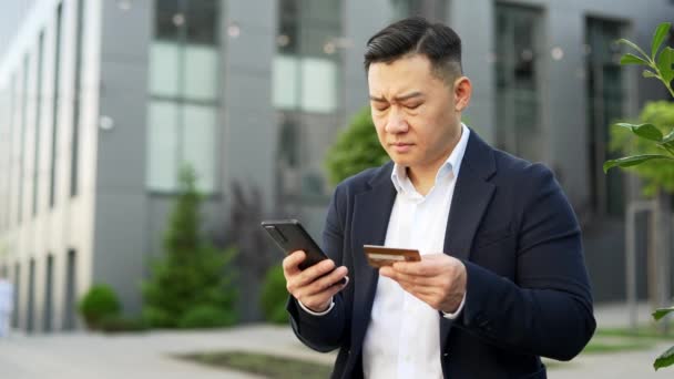 Impresionado Hombre Negocios Asiático Comprueba Tarjeta Crédito Teléfono Inteligente Pie — Vídeos de Stock