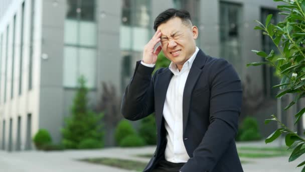 Azjatycki Biznesmen Garniturze Czuje Ból Głowy Siedząc Ławce Ulicy Pobliżu — Wideo stockowe