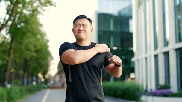 在城市的街道上 亚洲运动员在早晨跑步时感到剧烈的肩膀疼痛 这很让人不安 一名身穿运动服的悲哀男子受伤 一个不快乐的运动员在痛处擦拭和按摩肌肉 — 图库视频影像