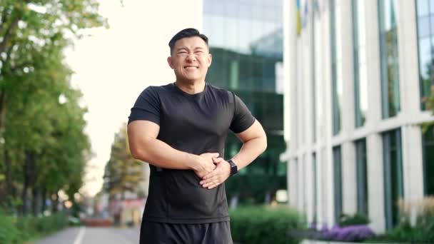 アジアのスポーツマンは 市街地で朝の走行中に右側に鋭い痛みを経験します 黒いTシャツの男性ランナーは 肝臓ボルトを持っています 痛みのアスリートガスは 彼の側を締めつける — ストック動画