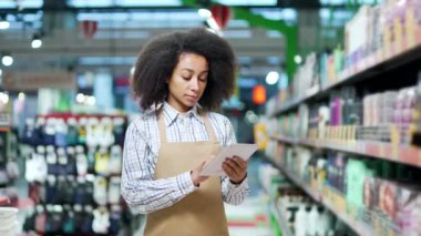 Elinde dijital tabletle önlüklü genç bir Afrikalı Amerikalı kadın süpermarket müdürünün portresi. Kendine güvenen kadın tezgahtar ya da süpermarket satıcısı Amera 'ya bakın.