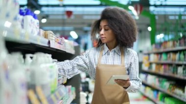 Afro-Amerikalı siyahi kadın, tablet üzerinde çalışan çalışan çalışan katip, kozmetik raflarının yanında duran ürünlerin durumunu kontrol eden yönetici süpermarkette ürün listesi envanteri yazıyor.