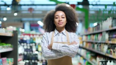 Markette çalışan kadın bir satıcının portresi. Kameraya bakıyor ve gülümsüyor. Markette önlüklü çalışan Afro-Amerikalı siyahi kadın çalışan. Kapalı alanda mutlu pozitif kız.