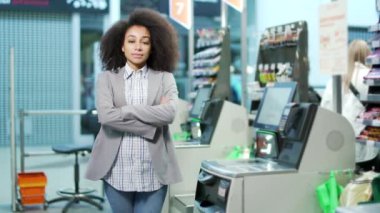 Süpermarkette portre genç bayan danışman satış elemanı self-servis kasasında duruyor ve kameraya bakıyor. Afrikalı Amerikalı siyahi kadın kasiyer mağaza çalışanı asistanı